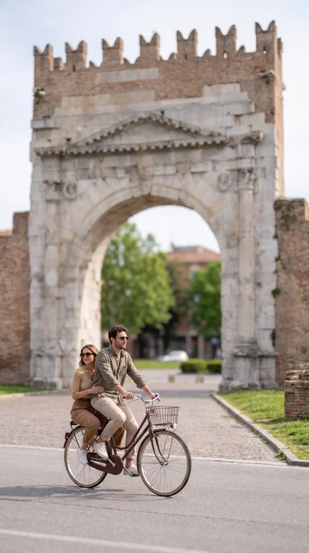 Coppia in bicicletta davanti all’Arco d’Augusto a Rimini