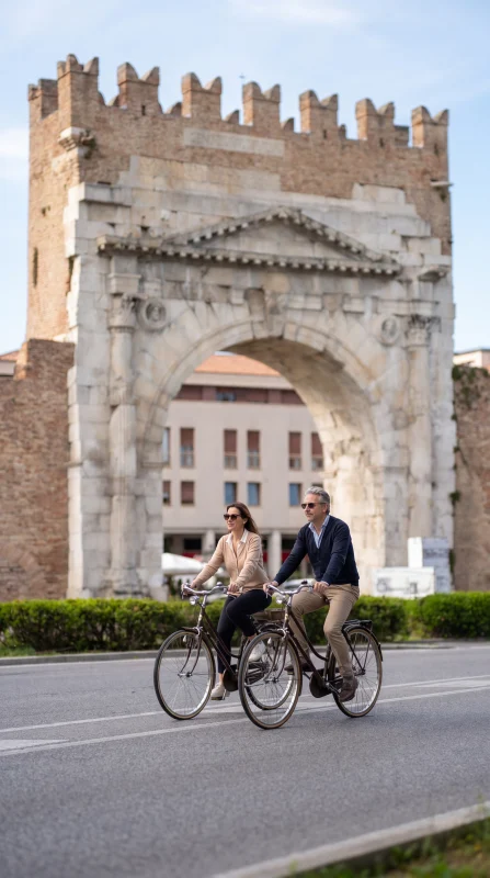 Coppia in bicicletta davanti all’Arco d’Augusto a Rimini