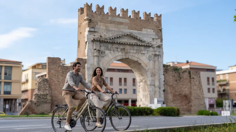Coppia in bicicletta davanti all’Arco d’Augusto di Rimini