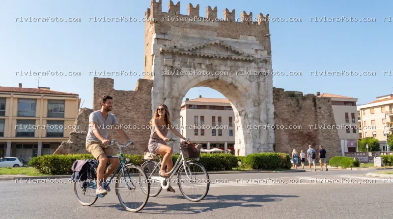Coppia in bicicletta davanti all’Arco d’Augusto a Rimini