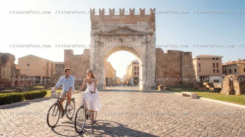 Coppia in bicicletta davanti all’Arco d’Augusto a Rimini