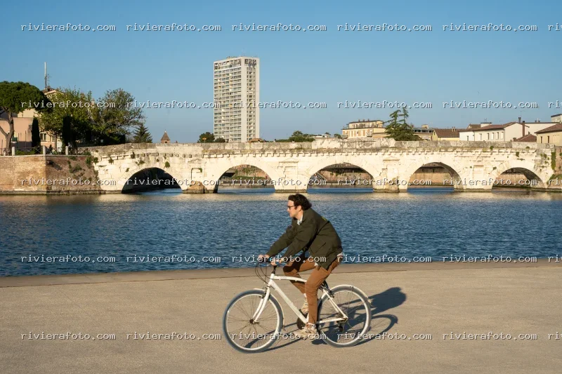 Ciclista al Ponte Tiberio con sfondo urbano di Rimini