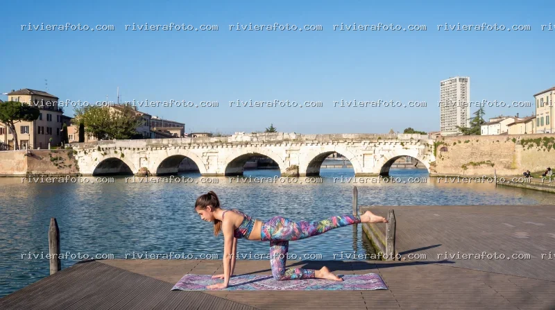 Yoga sul lungofiume con vista sul Ponte Tiberio a Rimini