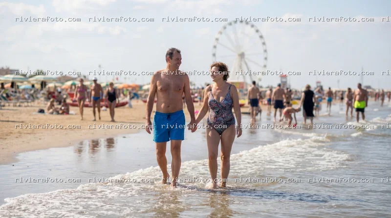 Coppia in passeggiata sulla spiaggia della Riviera Romagnola con ruota panoramica
