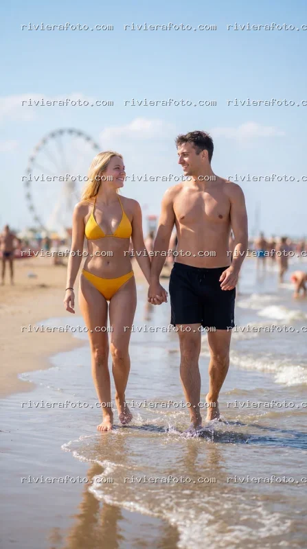 Coppia passeggia sulla spiaggia di Rimini con la Ruota Panoramica sullo sfondo