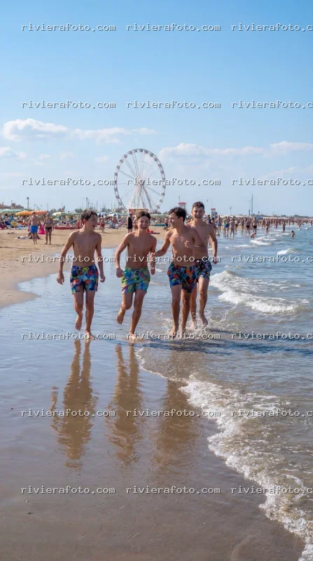 Giovani che corrono in spiaggia con Ruota Panoramica a Rimini